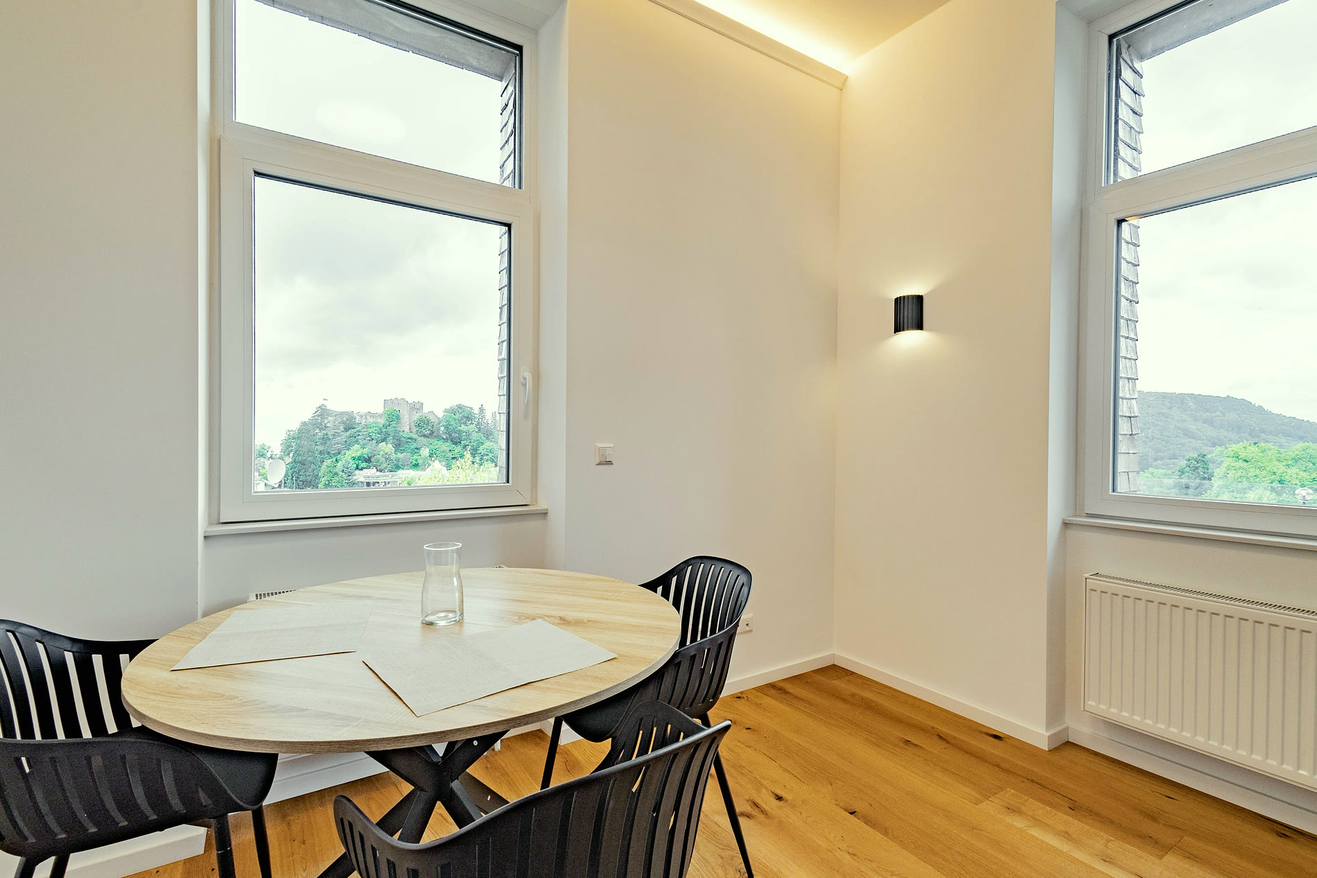 Esstisch vor zwei hohen Fenstern eines Apartments — im linken Fenster steht die Burgruine Badenweiler