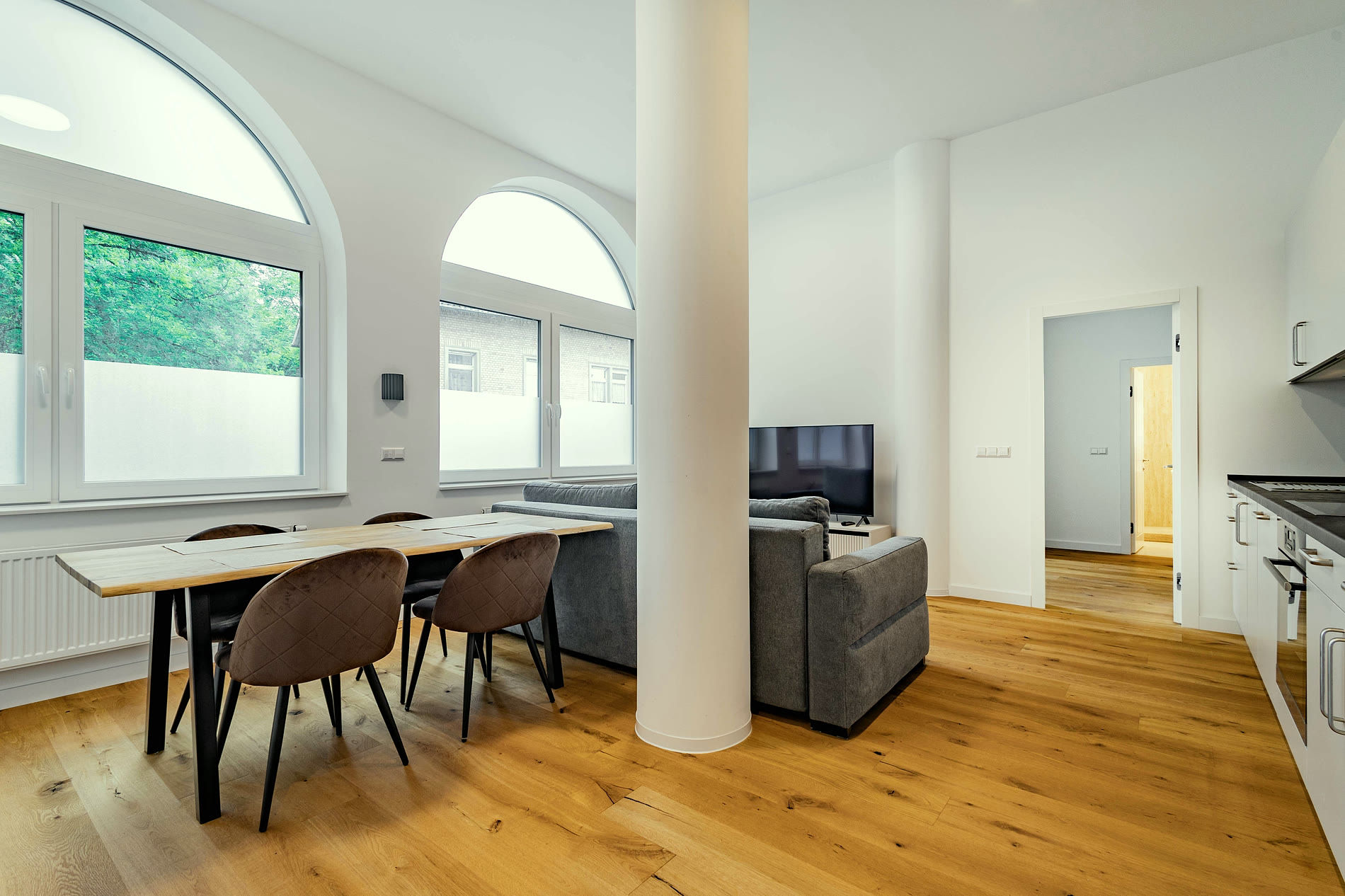 Wohnraum mit zwei Rundbogenfenstern, tragender Säule, Esstisch und Sofa auf Eichenparkett