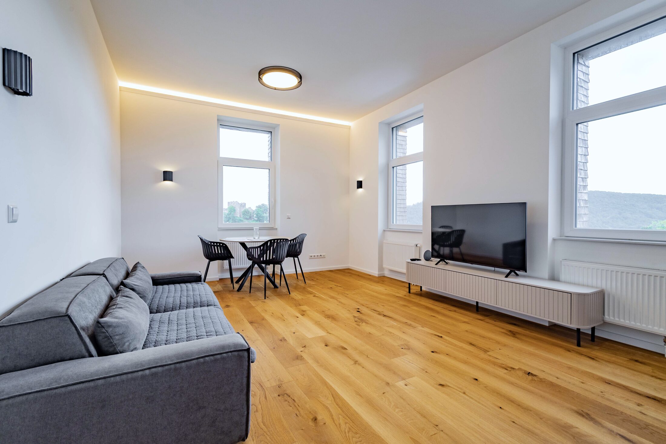 Heller Wohnraum mit Sofa, hohen Fenstern und Blick ins Grüne